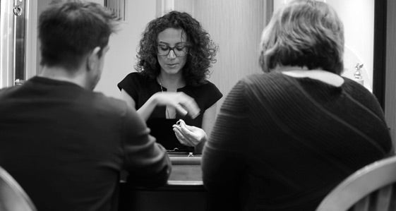 Black and white photo of a woman sitting at a table with two people, purchasing jewellery.