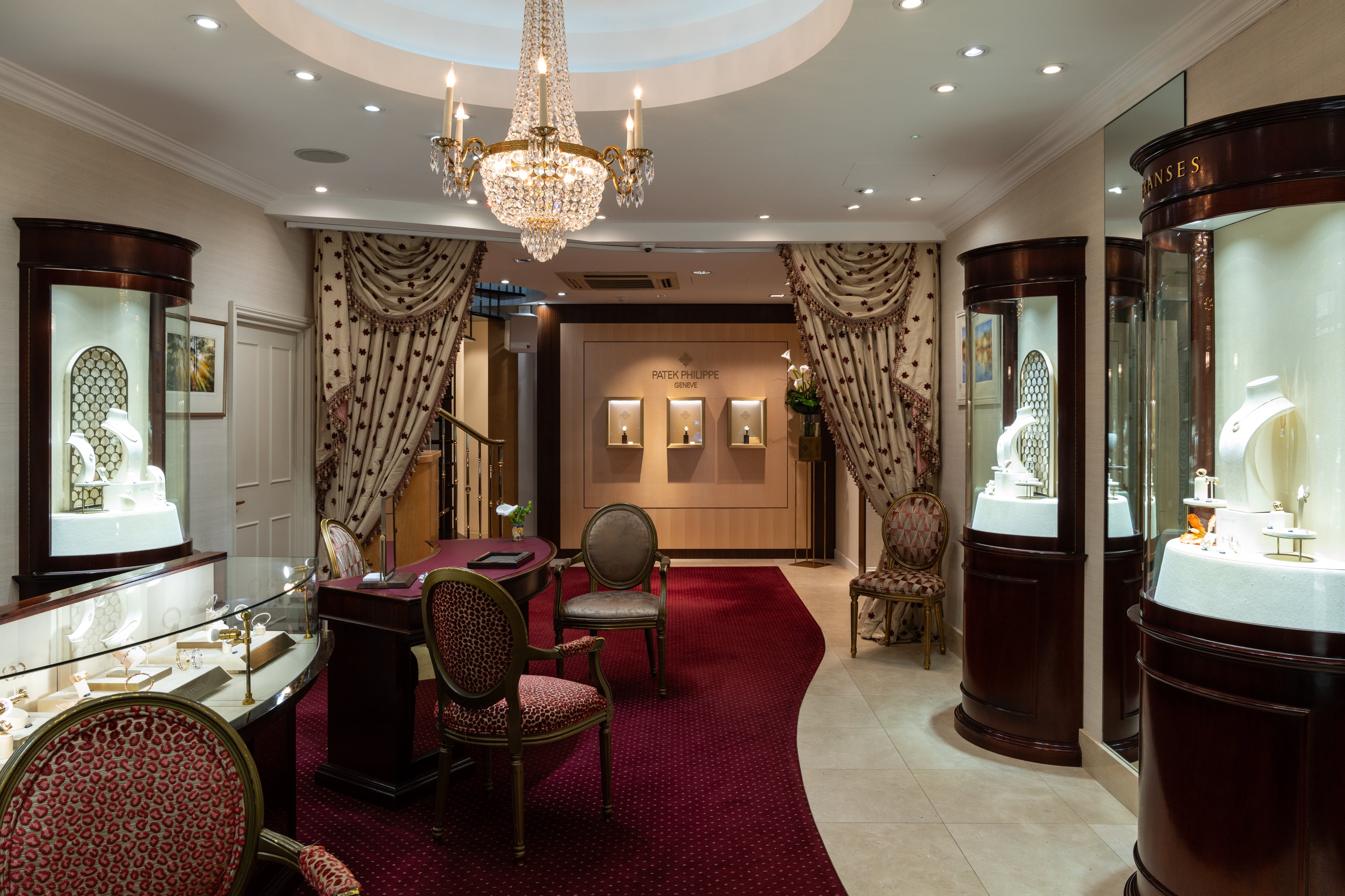 Luxurious interior of Patek Phillipe store with with chandelier, red carpet, and display cases.
