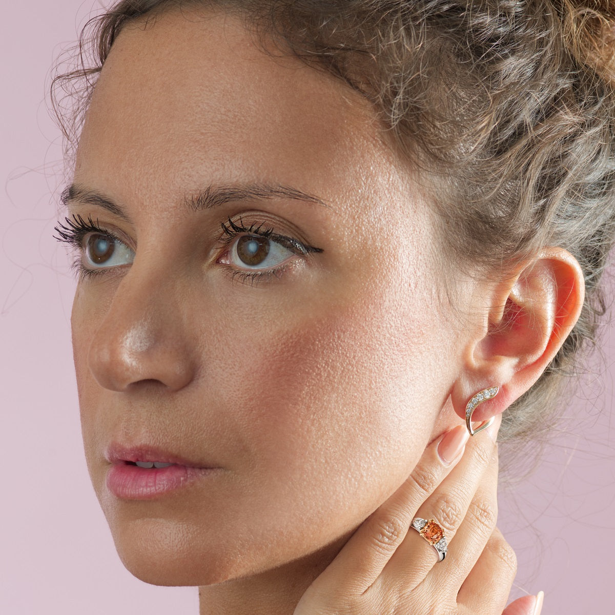 Close-up of a woman wearing earrings and a ring on a pink background