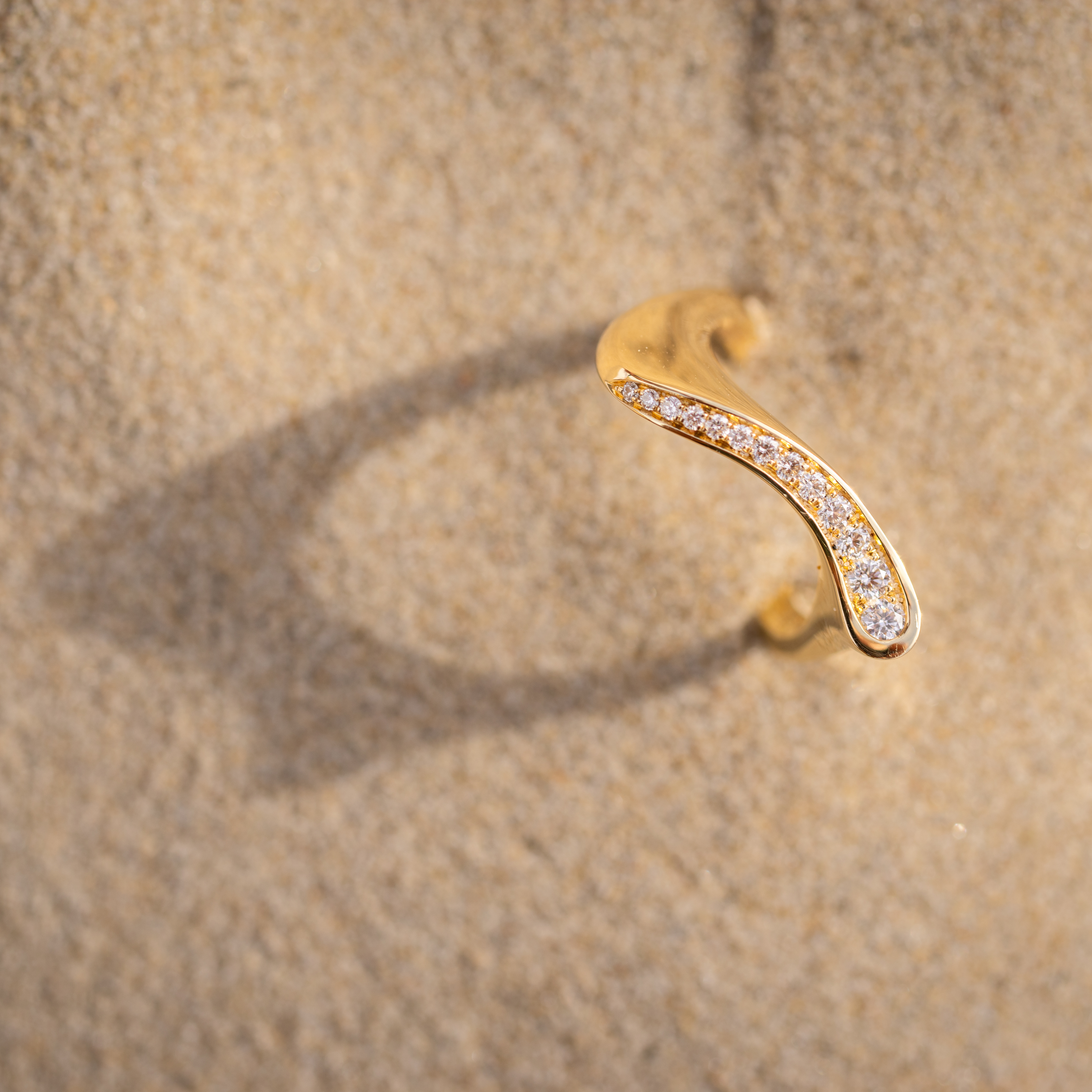 Gold earring with small diamonds on a beige textured background