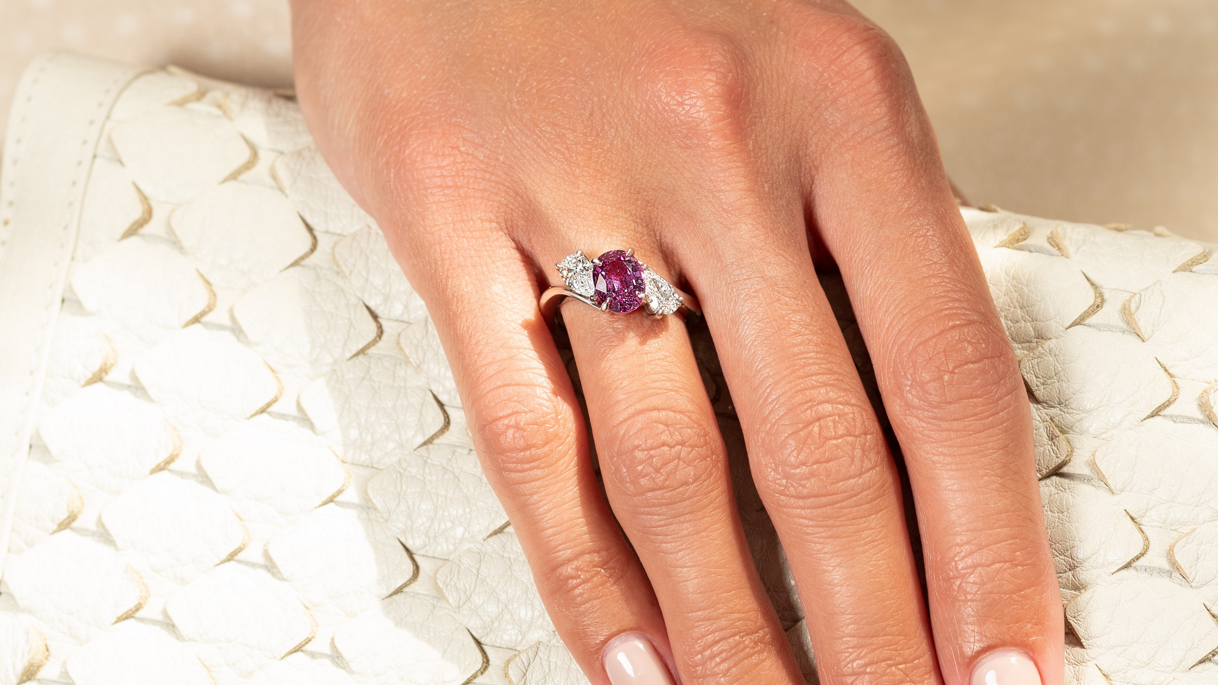 Hand wearing a ring with a pink gemstone on a textured beige surface
