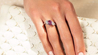 Hand wearing a ring with a pink gemstone on a textured beige surface