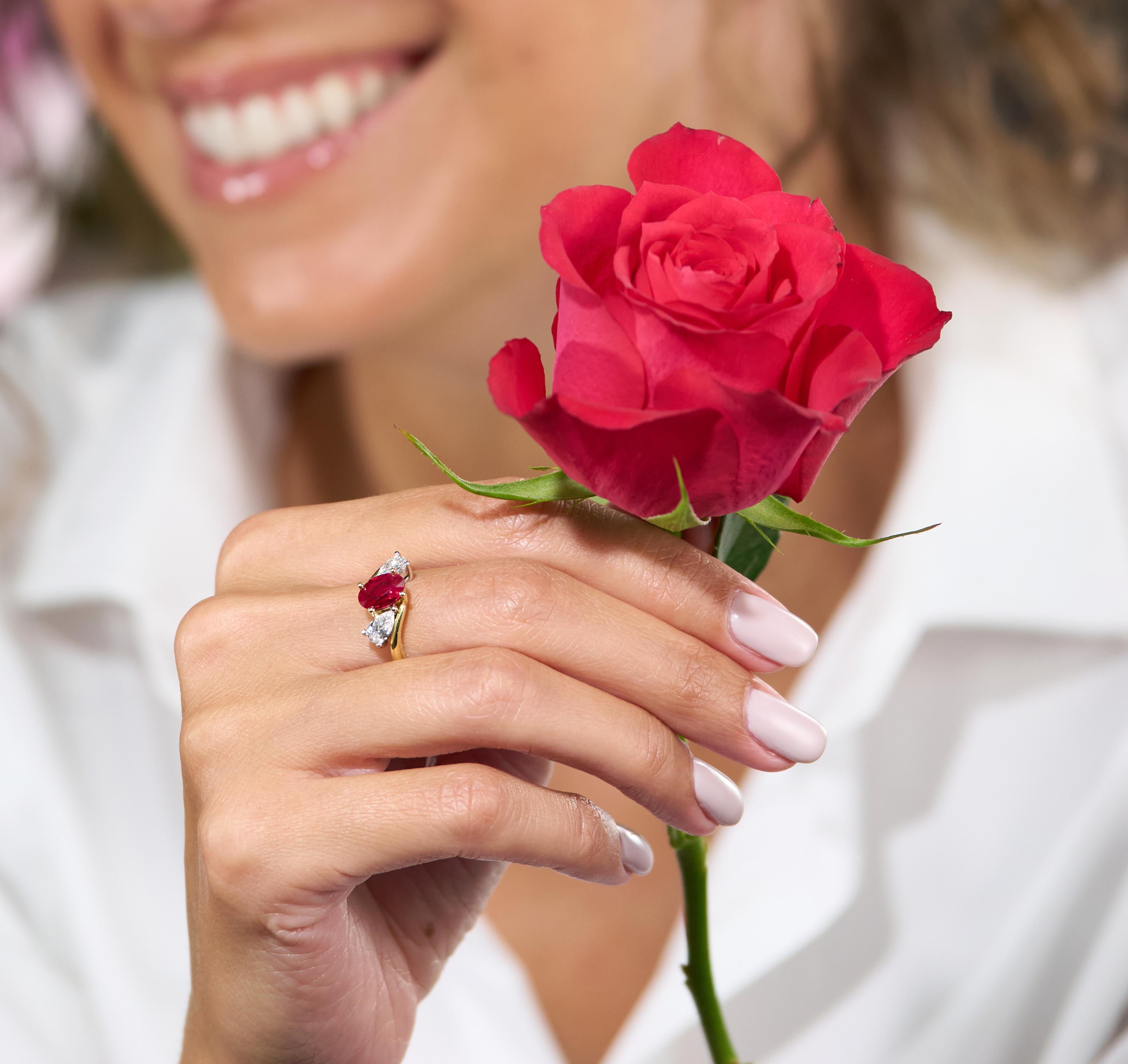 Person holding a red rose with a close-up of a hand wearing a ring featuring a ruby gemstone.