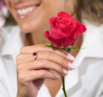 Person holding a red rose with a close-up of a hand wearing a ring featuring a ruby gemstone.