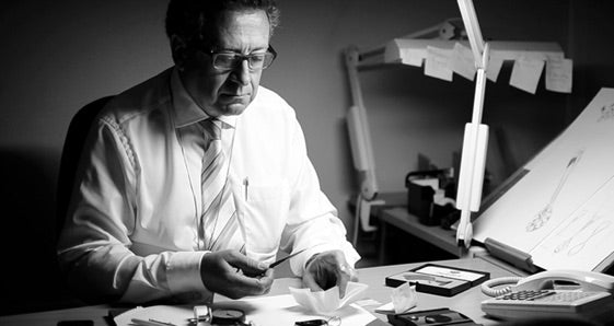 Man working at a desk with diamonds and tools in a dimly lit room.